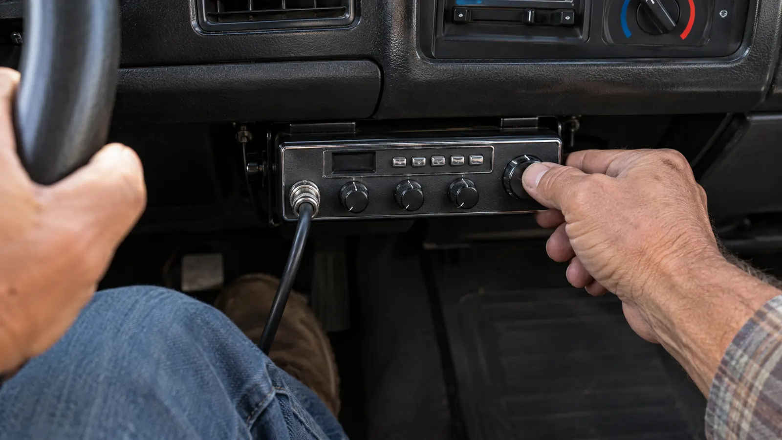 A hand reaching toward the controls of a mobile radio mounted under a dashboard