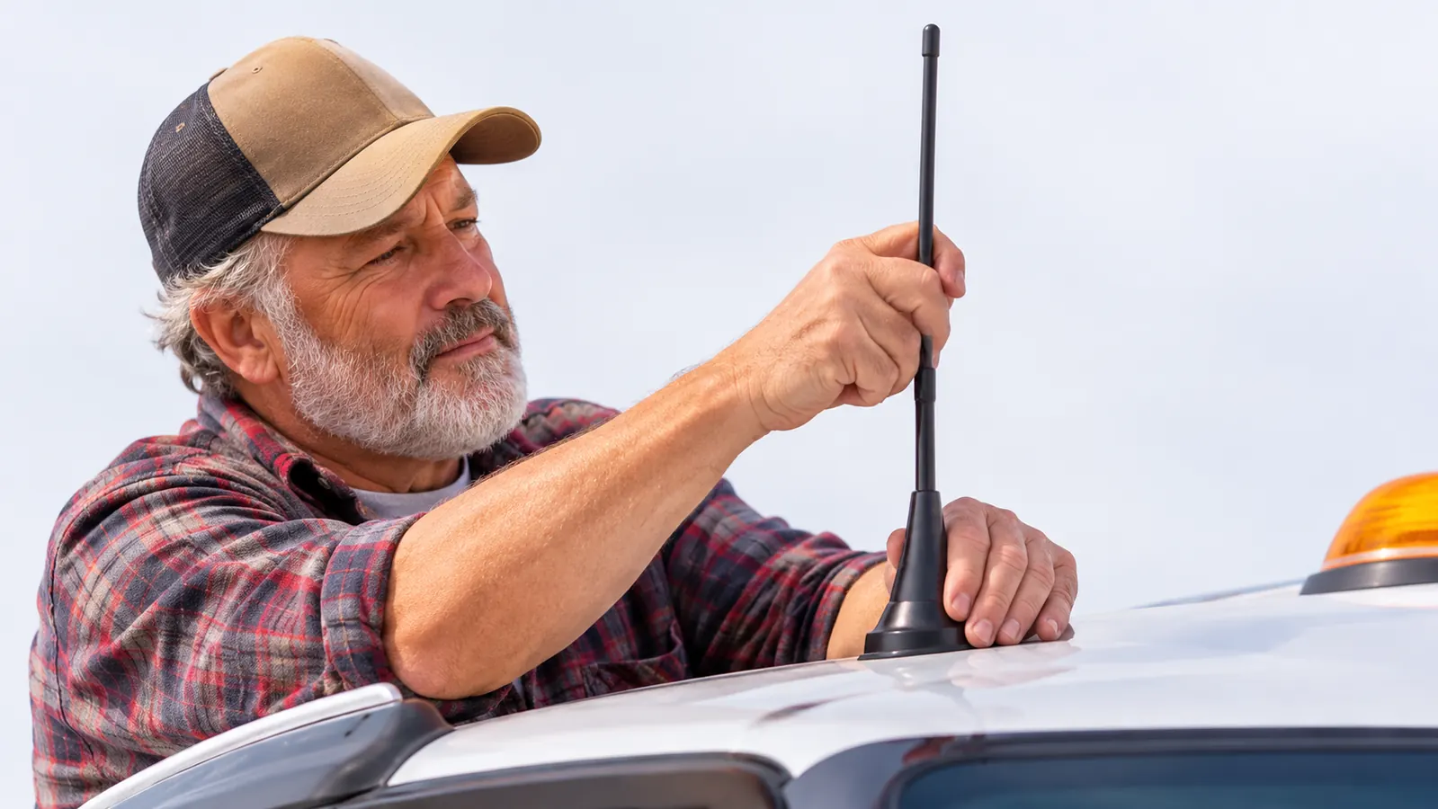 A hand checking the placement of a magnetic mount antenna on a truck cab roof
